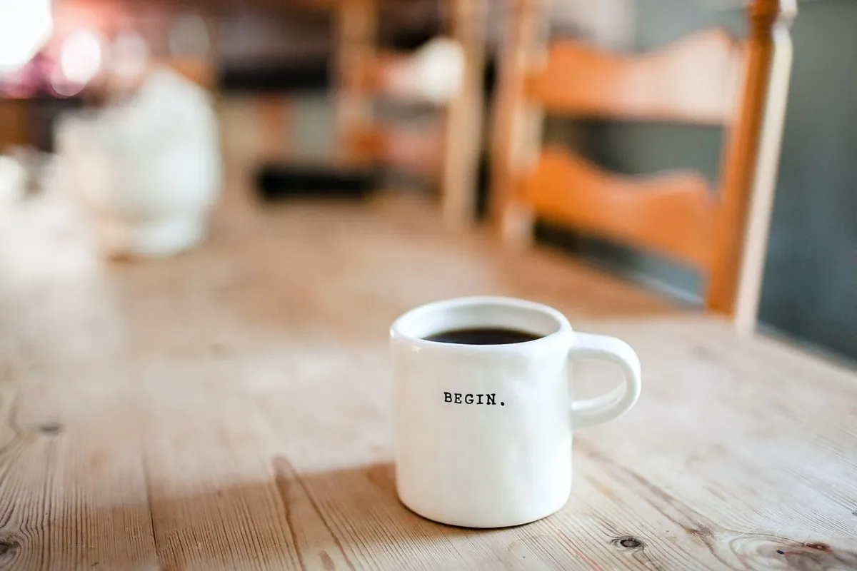 A coffee mug reading “Begin” on a wooden table