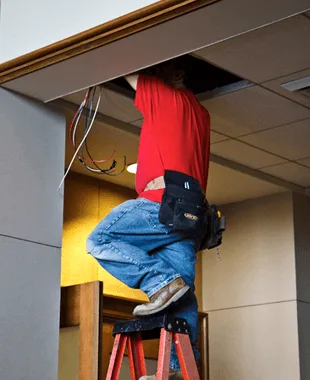 Electrician on a stepladder reaching up into a ceiling to run wiring