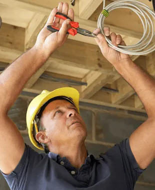 Electrician in a hard hat pulling wire through a ceiling